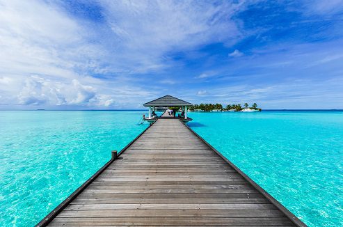 Tropical wooden pier leading to gazebo over turquoise ocean with clear blue sky.