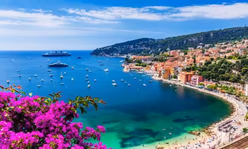 Scenic view of Villefranche-sur-Mer coastline with vibrant Mediterranean colors, yachts in the bay, and vivid purple bougainvillea in the foreground.
