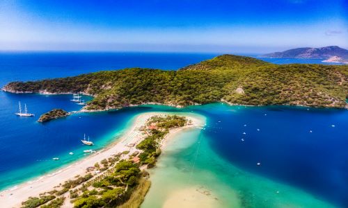 Aerial view of Ölüdeniz beach and stunning turquoise lagoon, surrounded by lush green hills and sailboats, in Turkey's Mediterranean coast.
