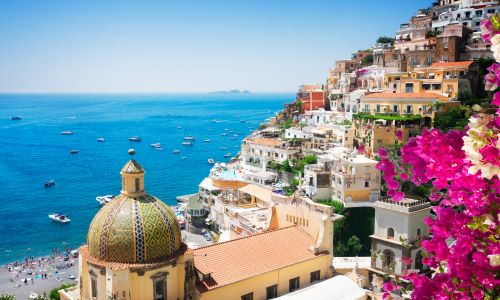 Scenic view of Positano on the Amalfi Coast, featuring colorful cliffside buildings, vibrant bougainvillea, and boats dotting the turquoise sea.
