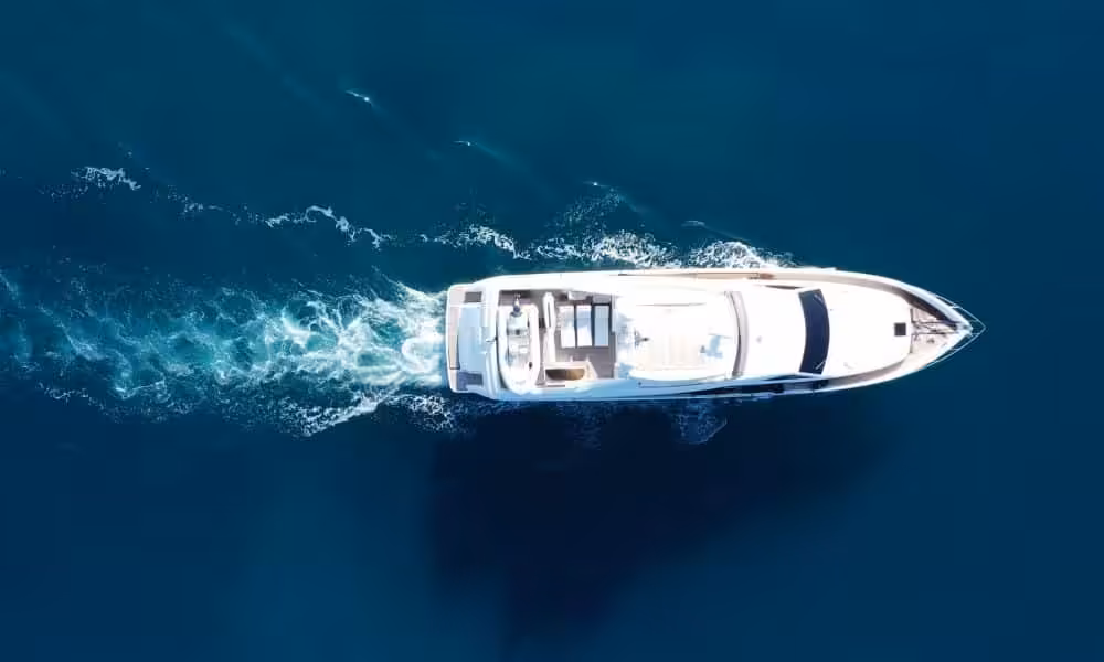 Aerial view of a luxury yacht cruising through clear blue ocean waters with visible wake trail.