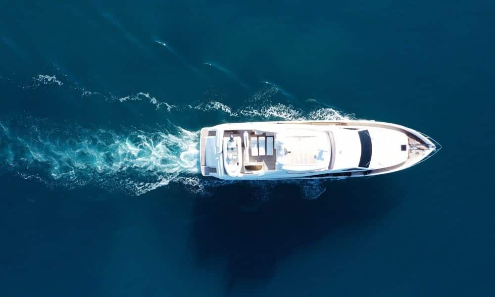Aerial view of a luxury yacht cruising through clear blue ocean waters with visible wake trail.