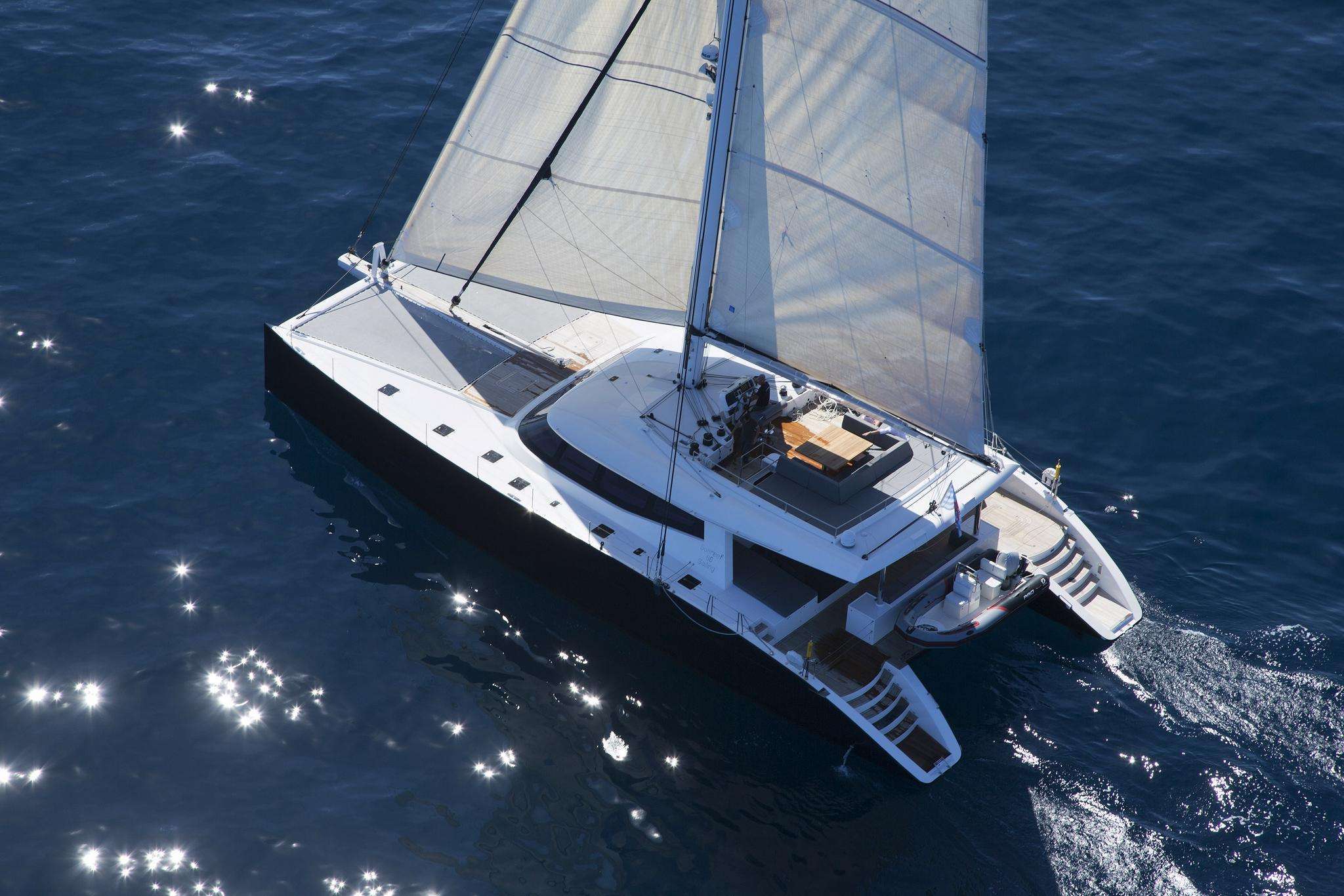 Luxury sailing catamaran cruising in clear blue ocean waters with sun reflecting on the surface, showcasing elegant design and spacious deck.