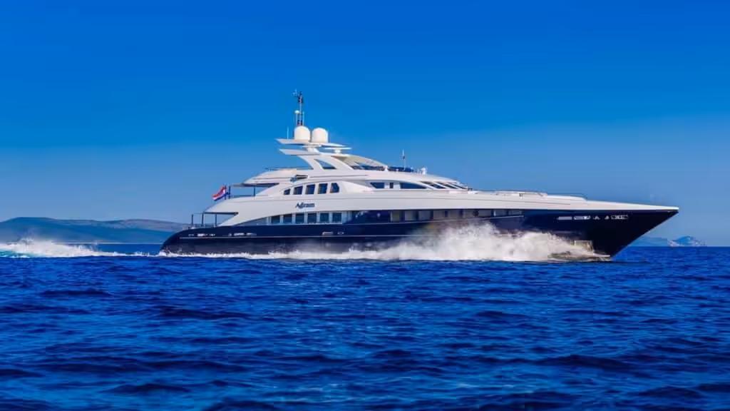Luxury yacht cruising on clear blue ocean with scenic coastline in the background under a sunny sky.