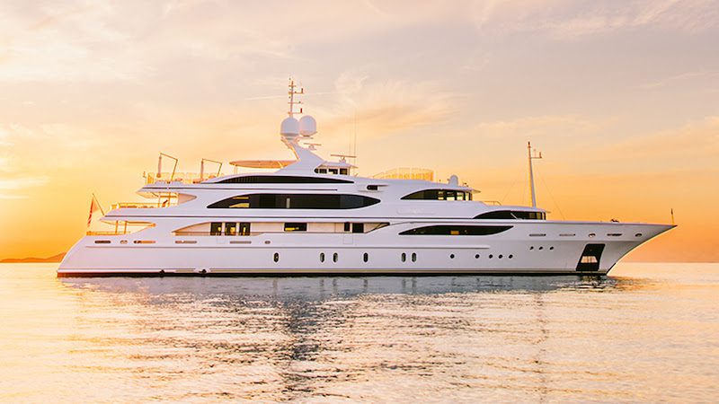 Luxurious white yacht sailing on calm sea during picturesque sunset, showcasing opulence and relaxation on the water.