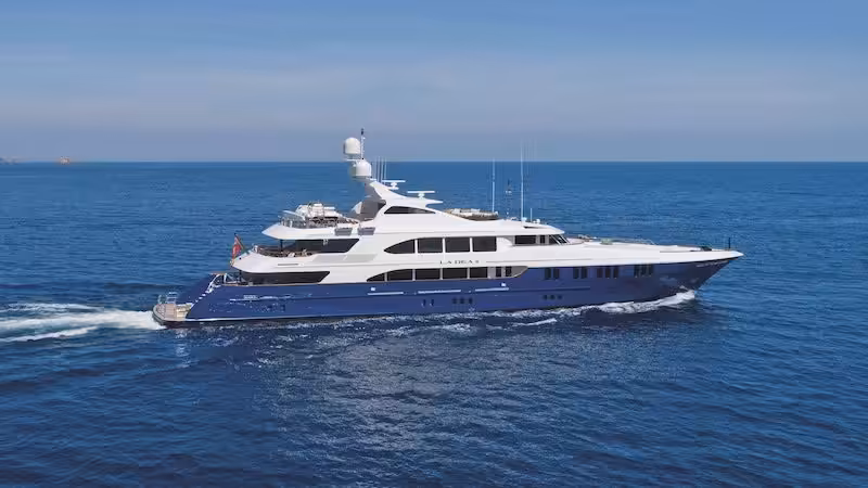 Luxurious white and blue yacht cruising on open sea under clear blue sky.