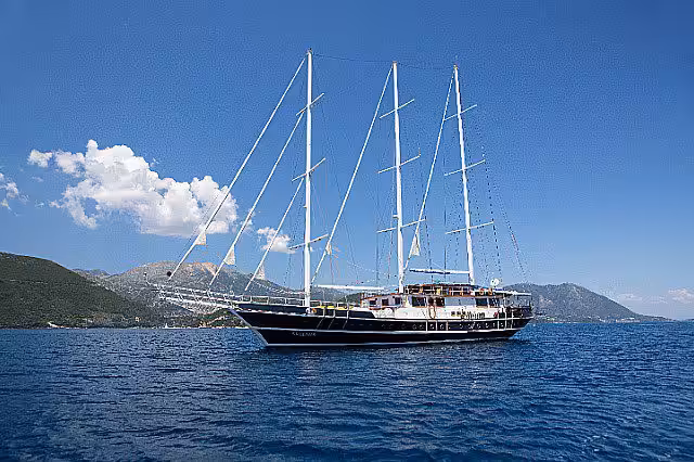 Luxury sailing yacht with multiple masts cruising on clear blue waters surrounded by scenic mountain landscape under a clear sky.