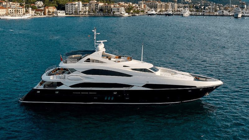 Luxury yacht cruising on clear turquoise water near coastal city marina with scenic buildings in the background