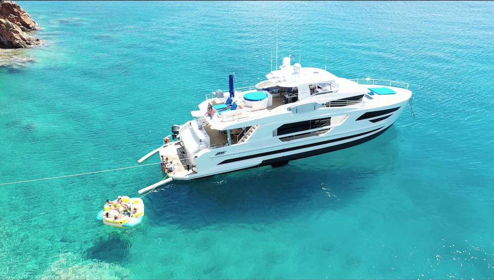 Luxury yacht anchored in clear turquoise waters with people enjoying a floating platform nearby, showcasing a serene marine leisure scene.