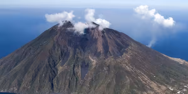 Aerial view of Stromboli volcano with plume of smoke rising, situated in the Aeolian Islands, Italy, surrounded by the blue Mediterranean Sea.
