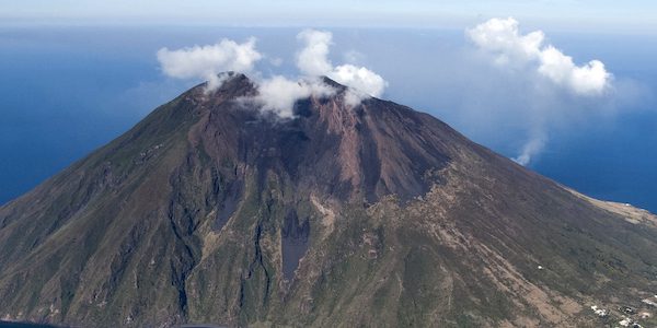 Aerial view of Stromboli volcano with plume of smoke rising, situated in the Aeolian Islands, Italy, surrounded by the blue Mediterranean Sea.