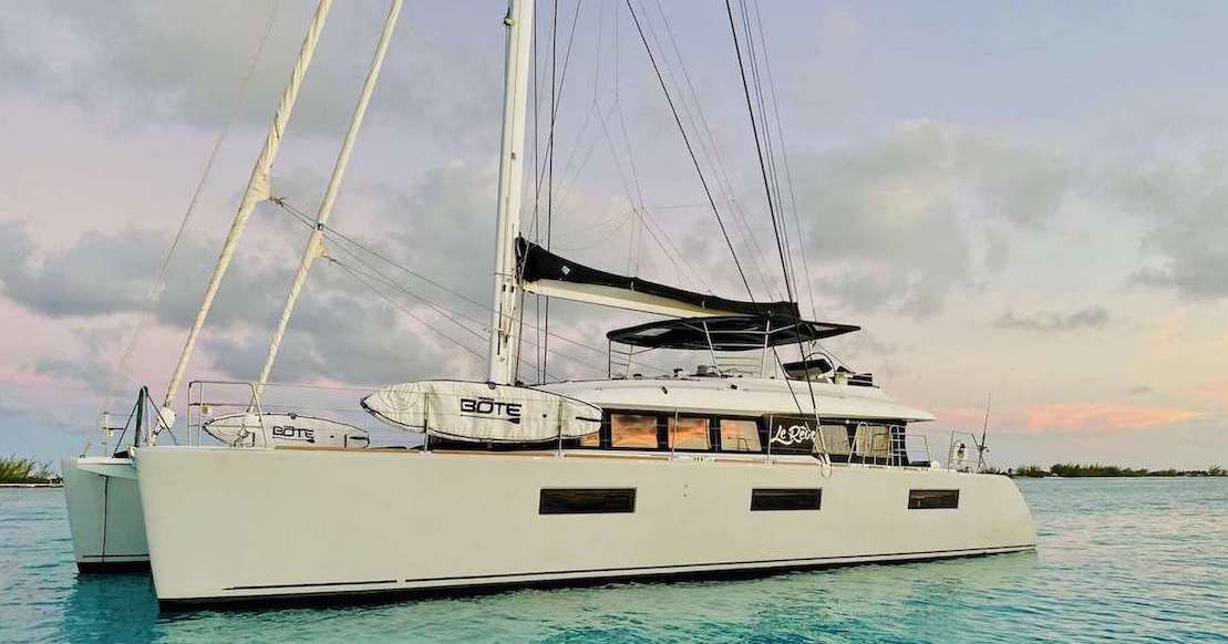 Catamaran yacht on calm ocean water at sunset with paddleboards, featuring a sleek design and modern sails.