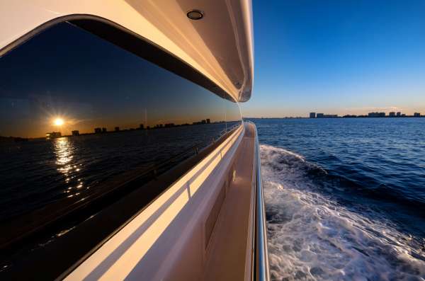 Luxury yacht cruising at sunset with city skyline and ocean waves, reflecting the vibrant evening sky.