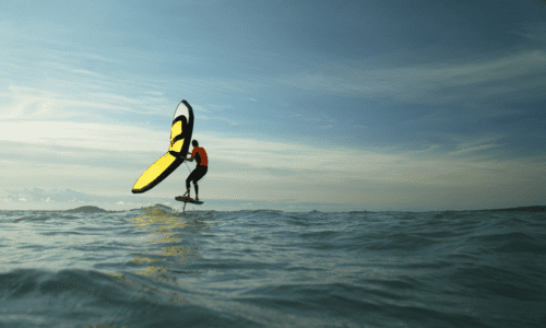 Person engaged in wing foiling on ocean waves under a clear sky.