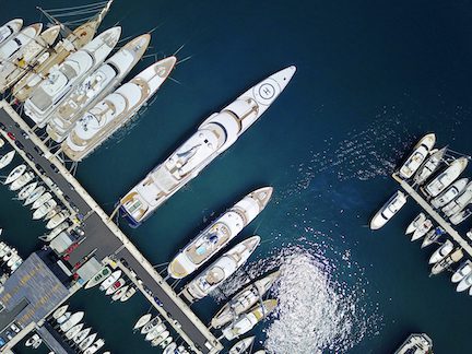 Aerial view of luxury yachts docked in a marina with shimmering water reflections.