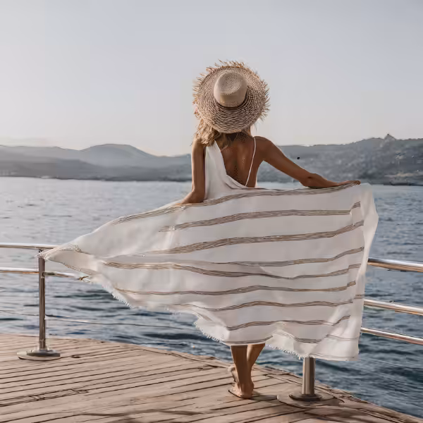 Woman in a white summer dress and straw hat standing on a pier by the ocean, enjoying the scenic coastal view