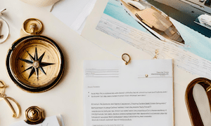 Vintage compass and documents on a desk alongside a yacht blueprint, representing navigation, exploration, and nautical design planning.