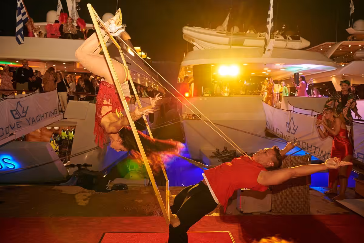 Acrobatic performance on a yacht with vibrant lights and an audience watching at a festive nighttime event.