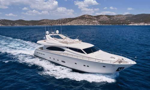 Luxury yacht cruising on clear blue waters with mountainous coastline in the background.