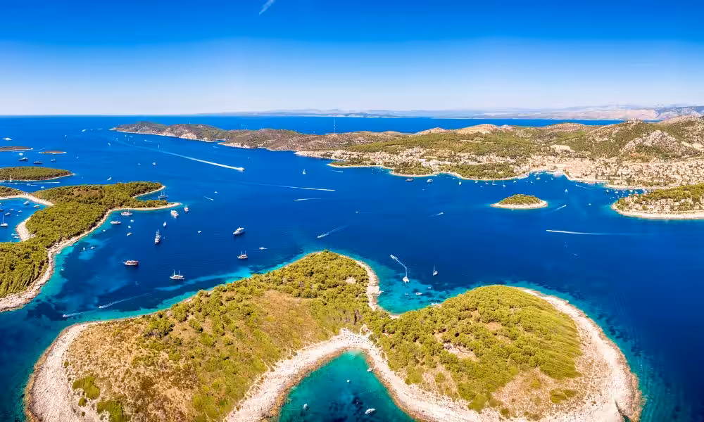 Aerial view of Hvar Islands in Croatia, showcasing turquoise waters, lush greenery, and numerous sailboats under a clear blue sky.