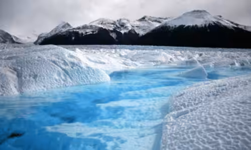 Majestic glacier landscape with icy blue water and snow-covered mountains in the background, showcasing natural beauty and climate change effects.