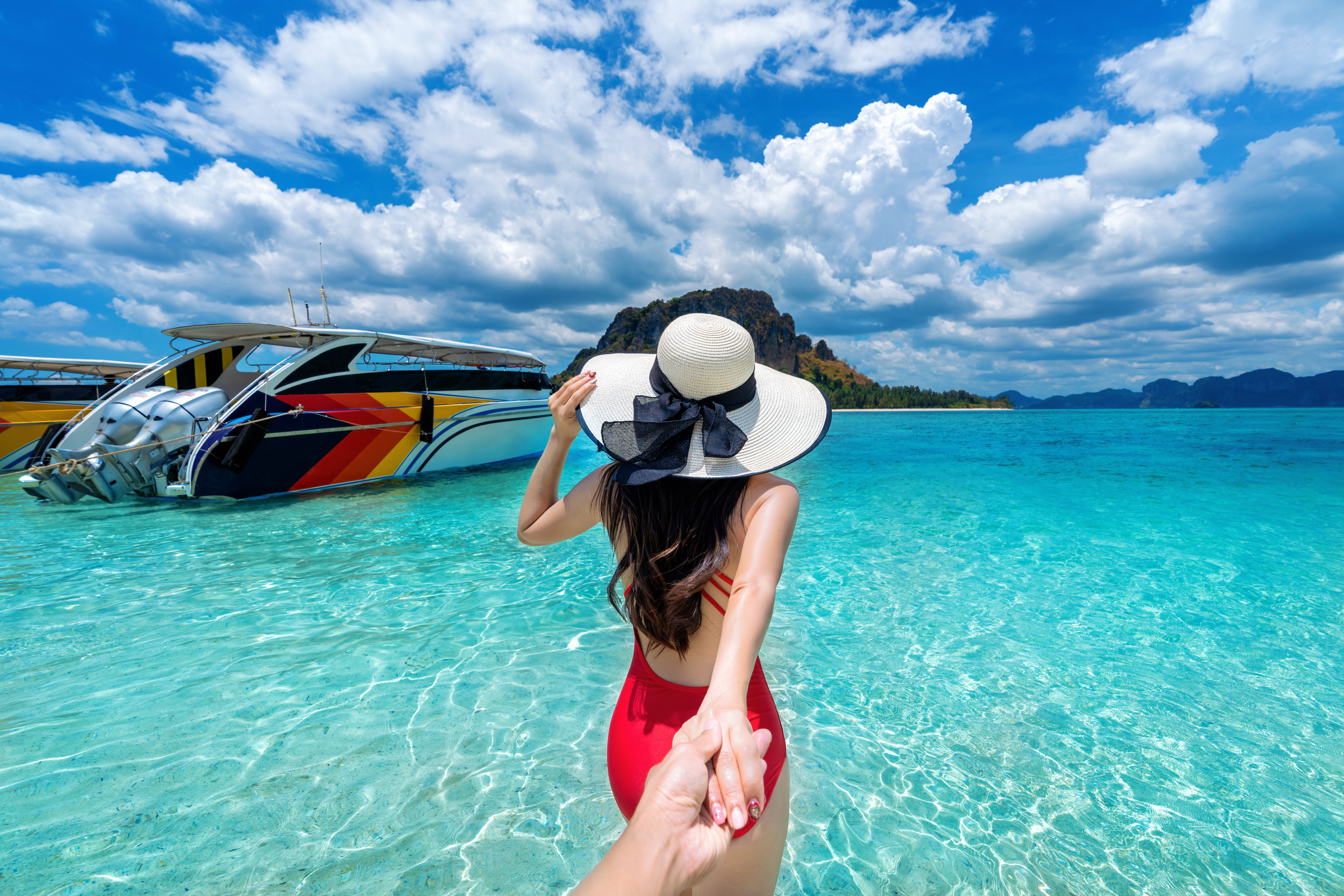 Bikini girl holding man's hand and leading him to ocean in Krabi, Thailand.